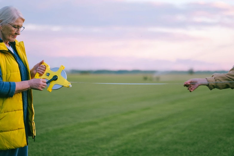 an older man in yellow jacket pulling string of a kite