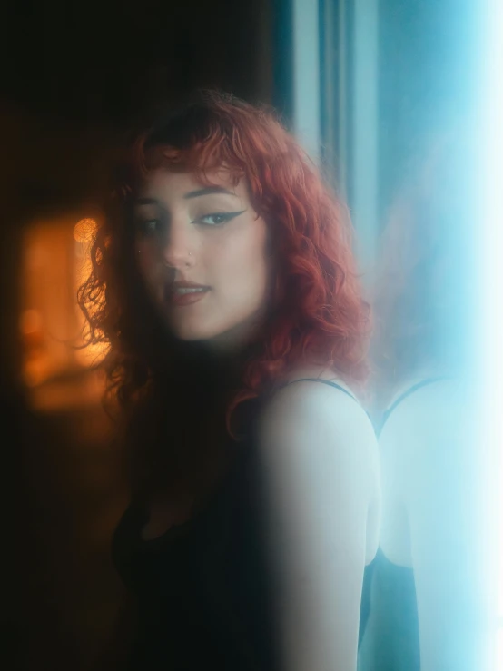 a woman with red hair and bright red curls, looks towards the camera