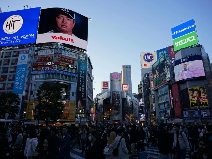 a crowded city square during the daytime with billboards and buildings