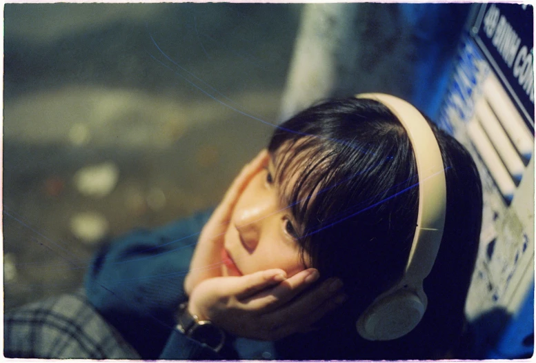 an asian woman sitting next to a wall wearing headphones