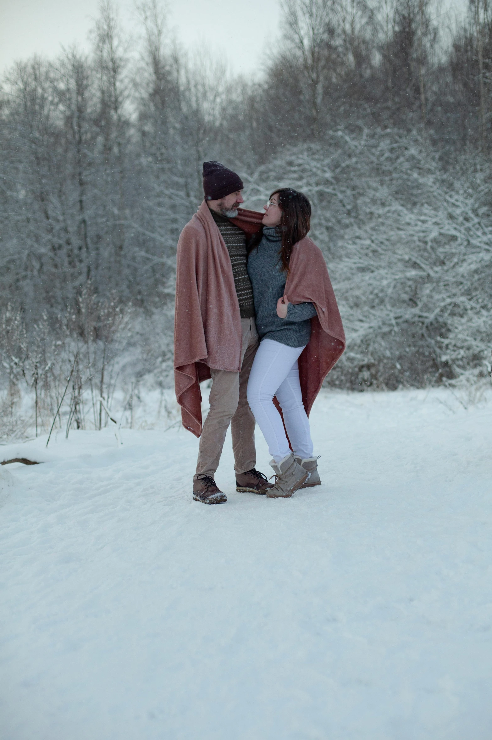 a couple in a blanket hugging on a snowy day