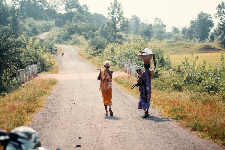 three people walking down a road carrying pots on their head