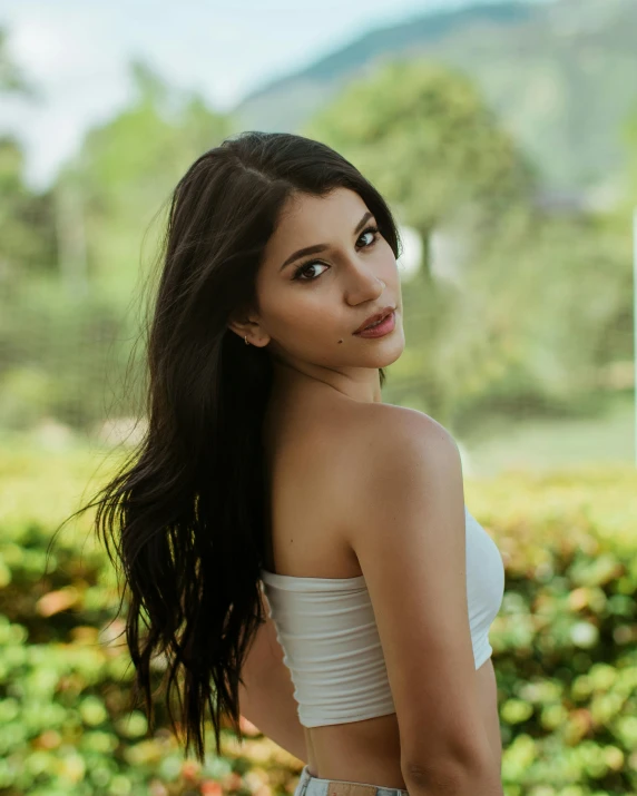 a woman standing next to shrubbery wearing a white top