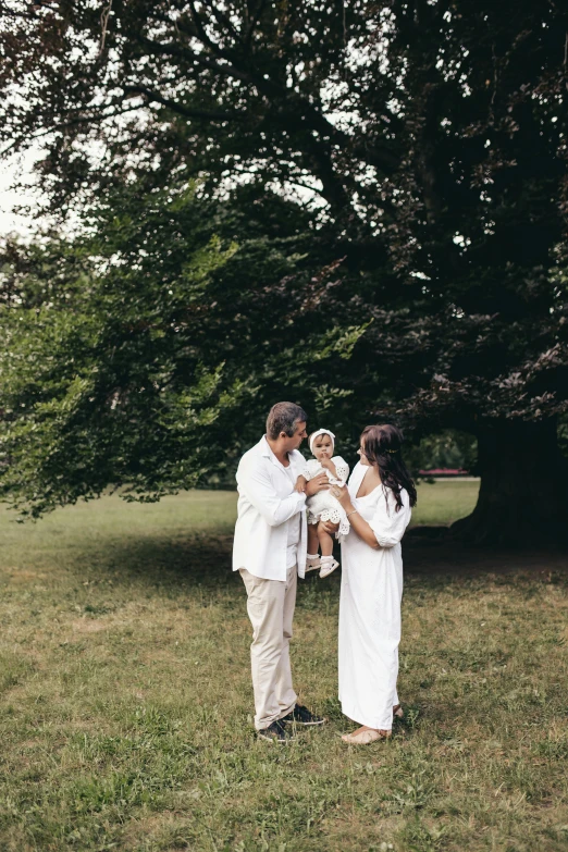 a bride and groom holding a child in the grass