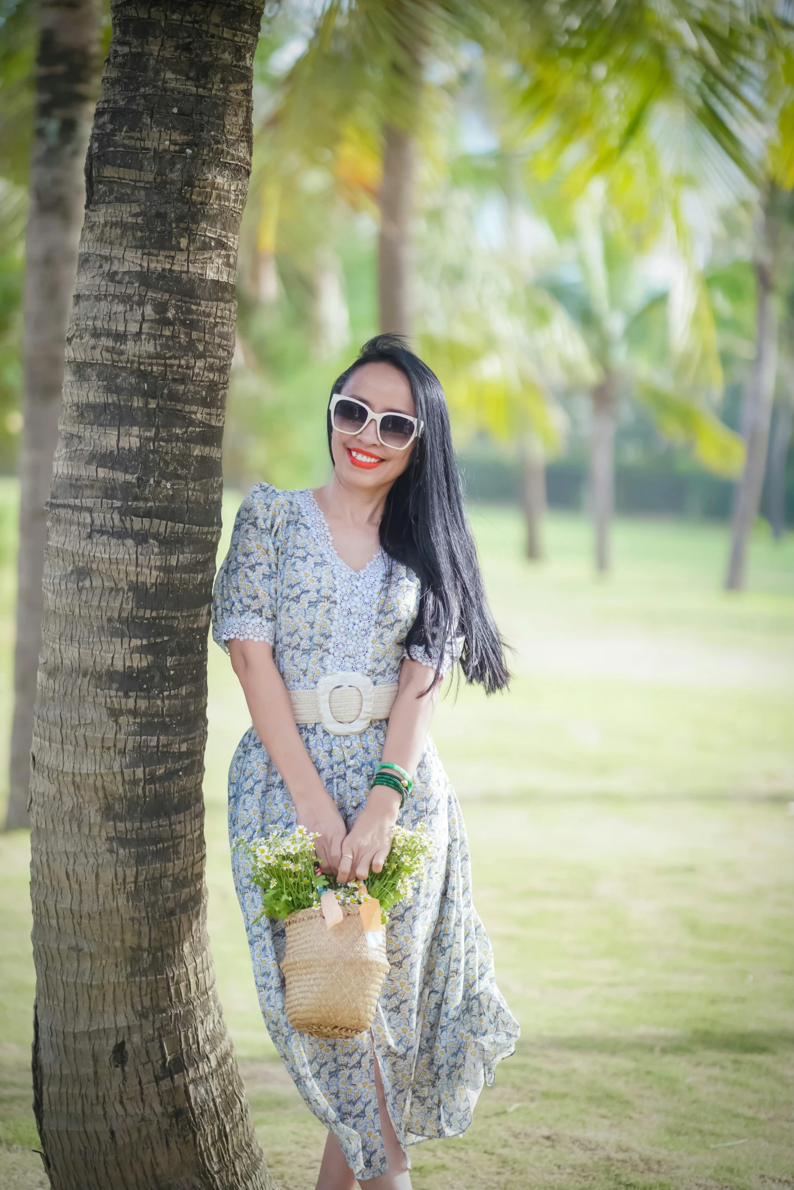 woman posing by a tree in sunglasses with her bag