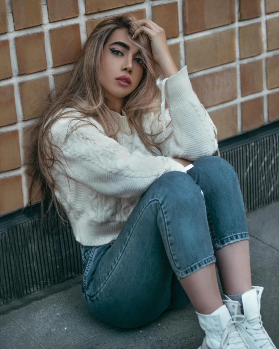 a woman wearing sneakers is posing against a brick wall