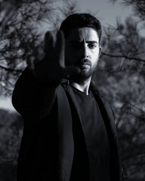 man in a dark suit standing under trees