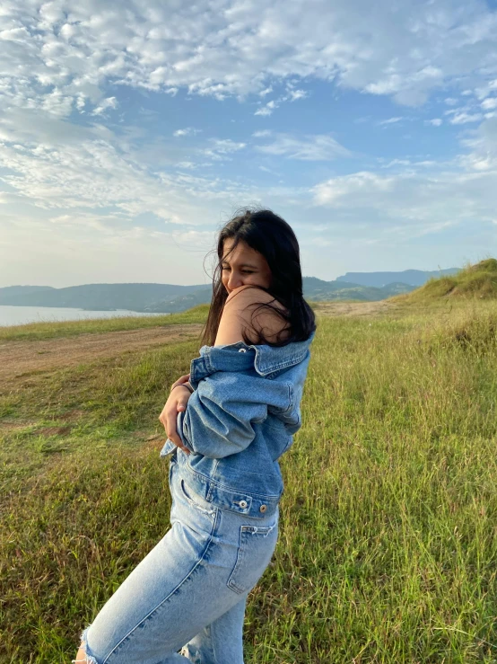 a girl in a jean jacket is in the grass and her pants are out