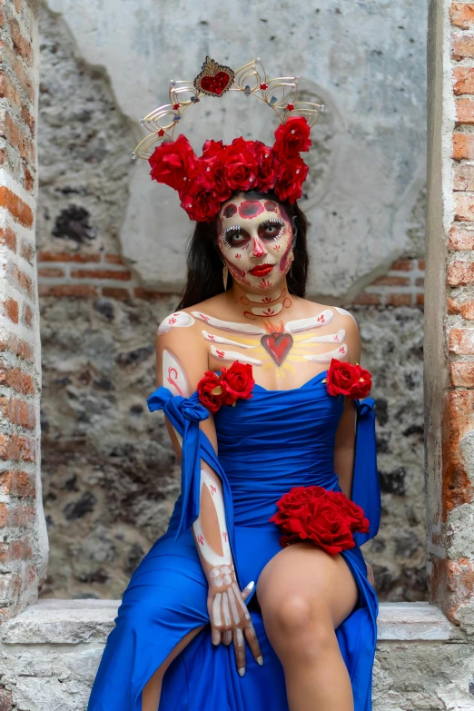 a woman sitting down in front of brick walls wearing a blue gown and floral headpiece