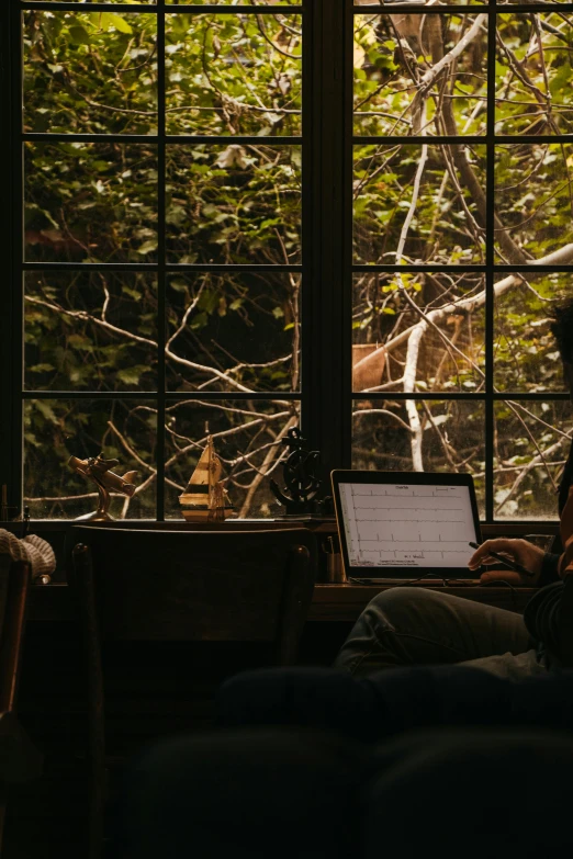 person sitting on their laptop at a window sill