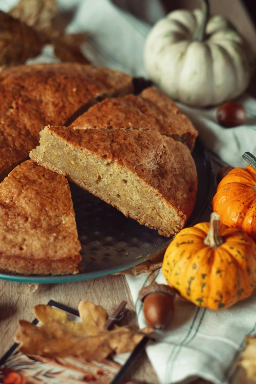 a pie is on a platter with small pumpkins next to it