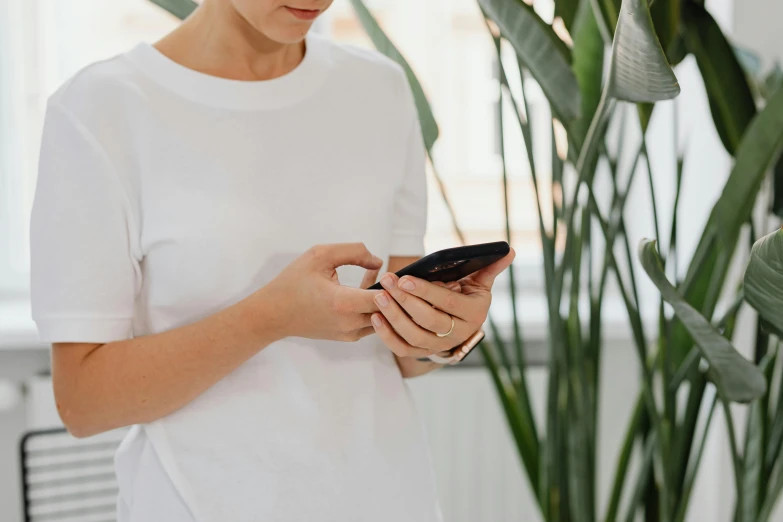 a woman is using her phone while leaning against a tall plant