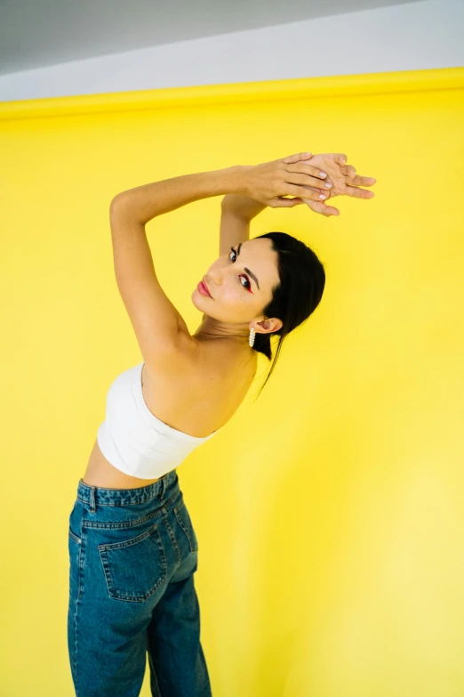 a woman stands against a yellow wall