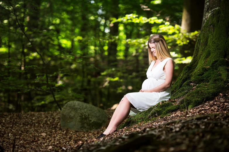 a pregnant woman sits on a mossy mound in the forest