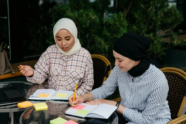 two women sitting down at a table with some pens and notebooks