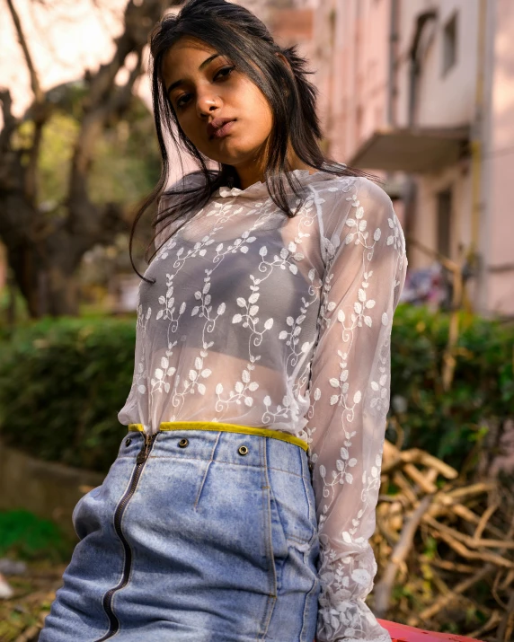 the woman is wearing an embroidered top and denim skirt
