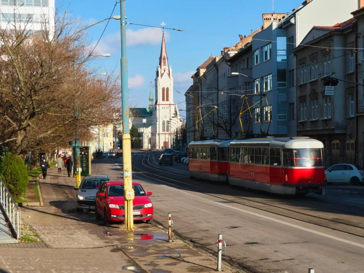 the road is empty and has a red car parked along with a red and white tram