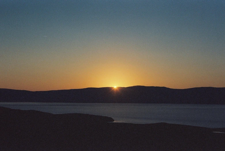 the sun rising over a lake, as seen from the top of a hill