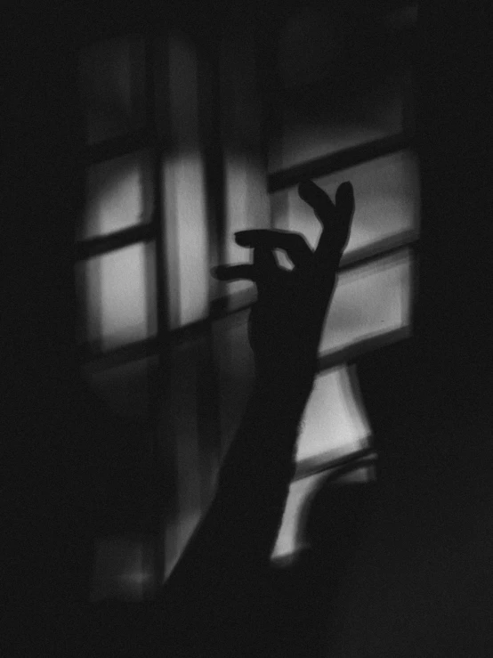 silhouetted hand reaches for the window in a dark room