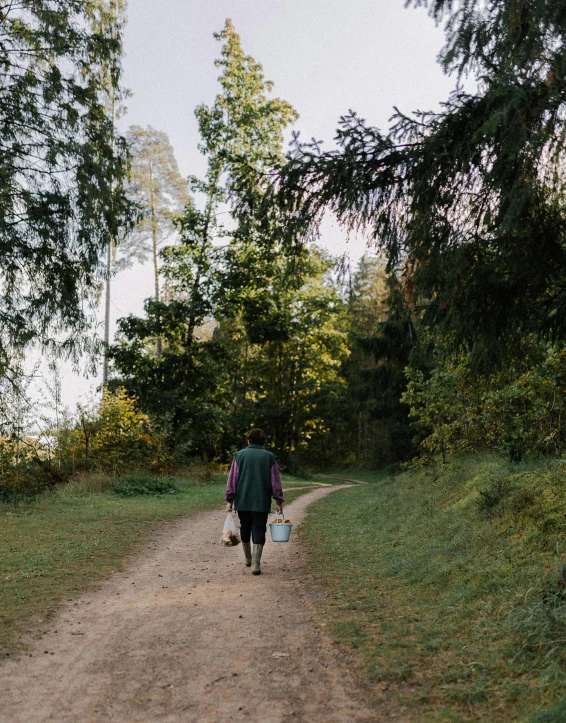 a person carrying a small blue bag while walking down a dirt road