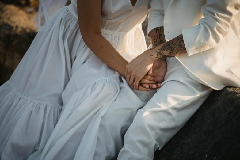 a couple holding hands holding their fingers and wearing white wedding gowns