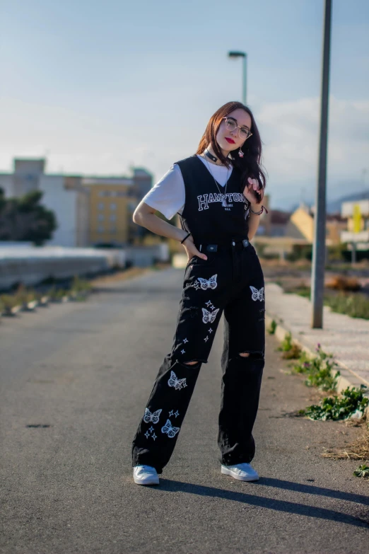 a woman with glasses, black overalls and white sneakers