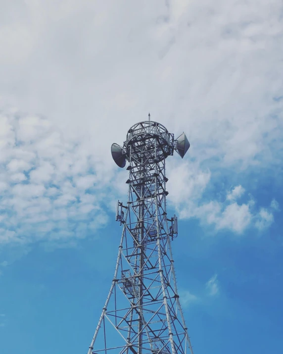 the cellular tower is seen under blue skies with clouds