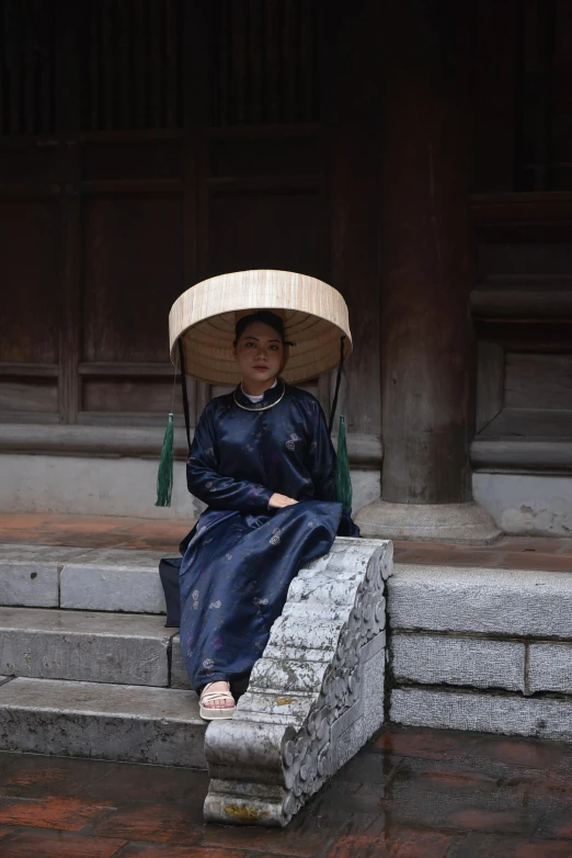 a woman wearing a traditional conical hat sitting on steps