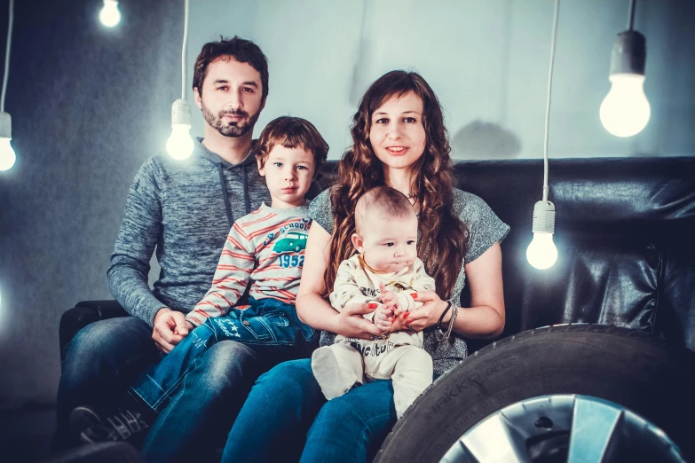 a family with two children sitting on a couch, some lights overhead