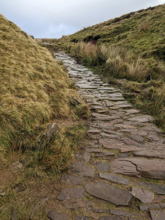 an old stone path is going up the grassy hill