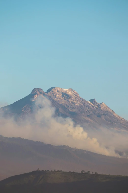 smoke rises from a cloud filled mountain on a clear day