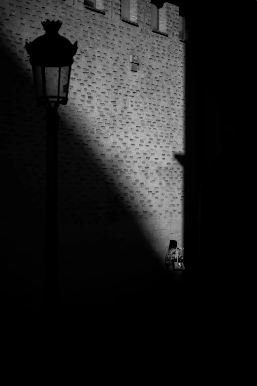 a lamp post is in the dark and shadow from a wall with the corner wall of bricks and a wallpapered area with the floor