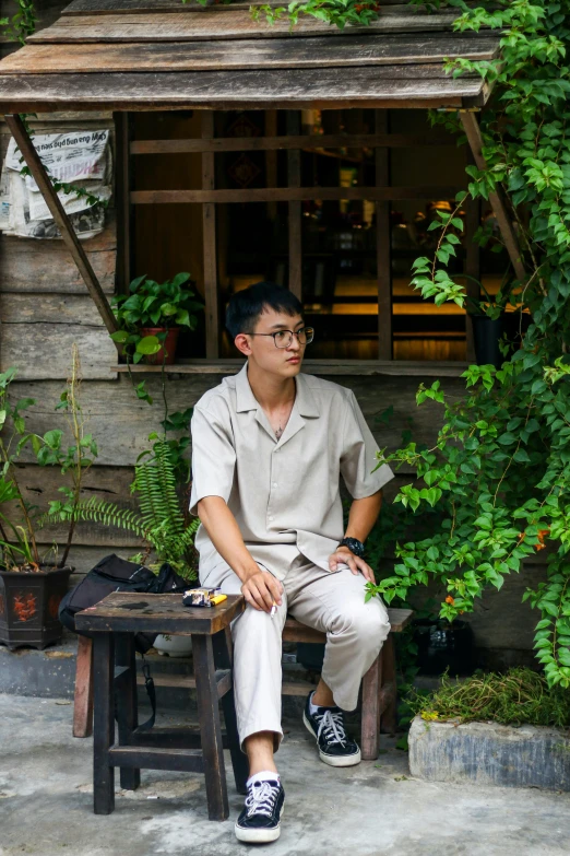 an asian man sitting on a bench near some plants