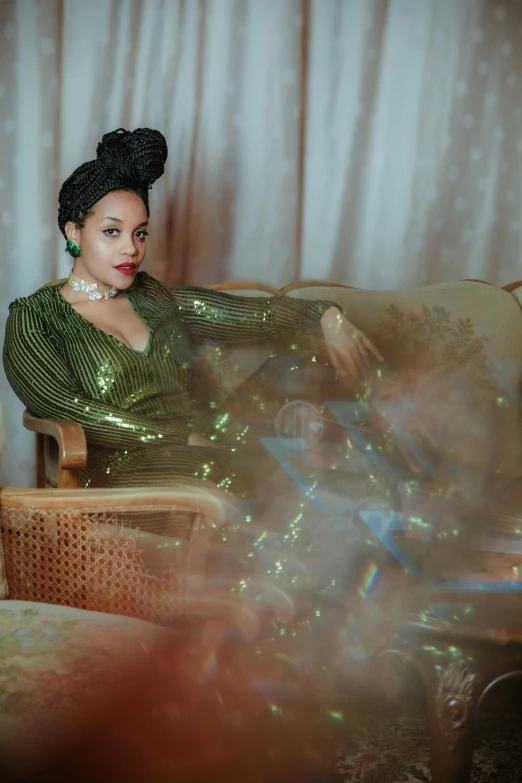 a woman sits on a couch and wears a green dress
