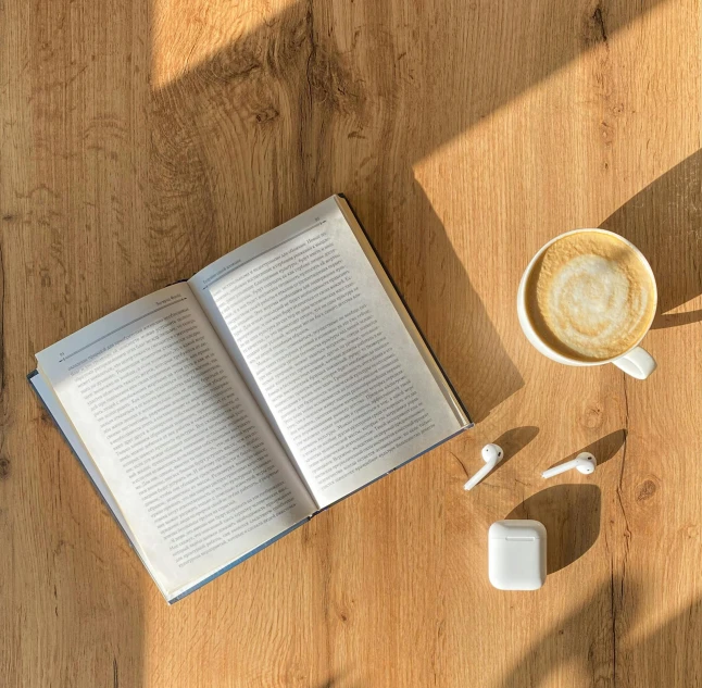 an open book on a wooden table next to a cup of coffee