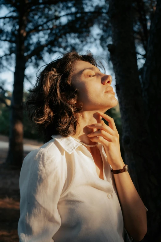 woman in a white shirt standing in front of trees looking up