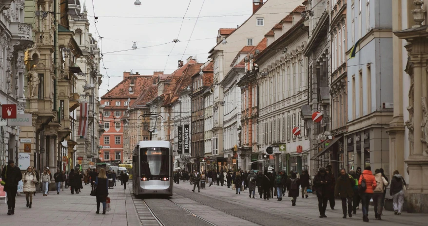 people walk along a city street as a tram is coming down the street