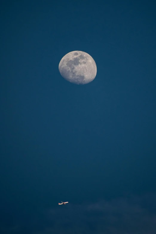 a airplane flying past the moon with a clear sky