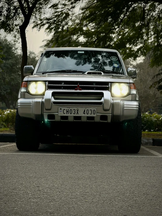 the silver truck has headlights on and it is parked in the street