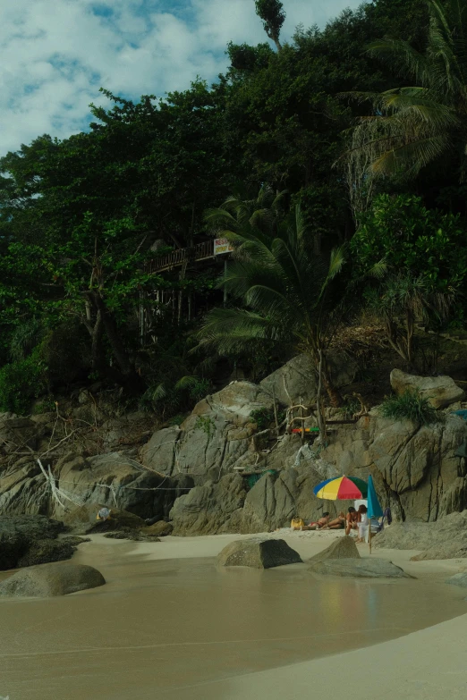 people at the beach under a multi - colored umbrella