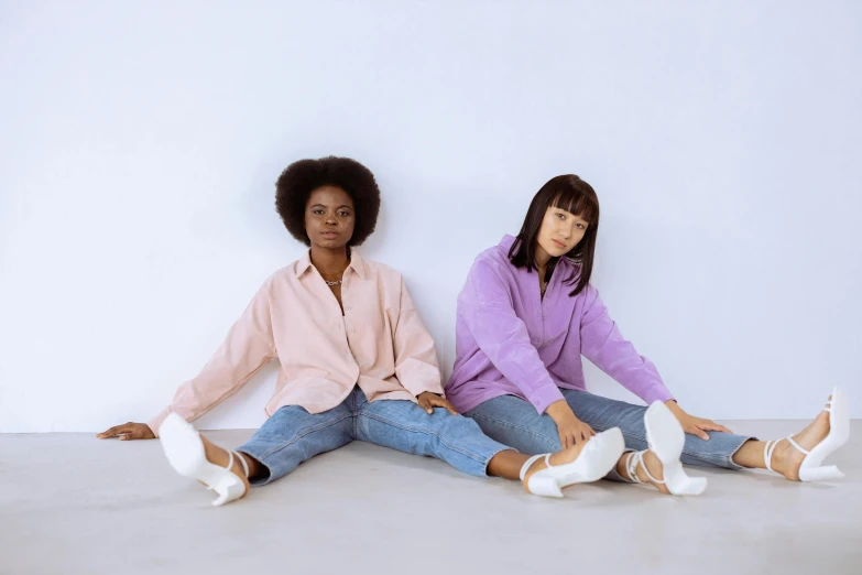 two women sit on the ground, looking at the camera and smiling