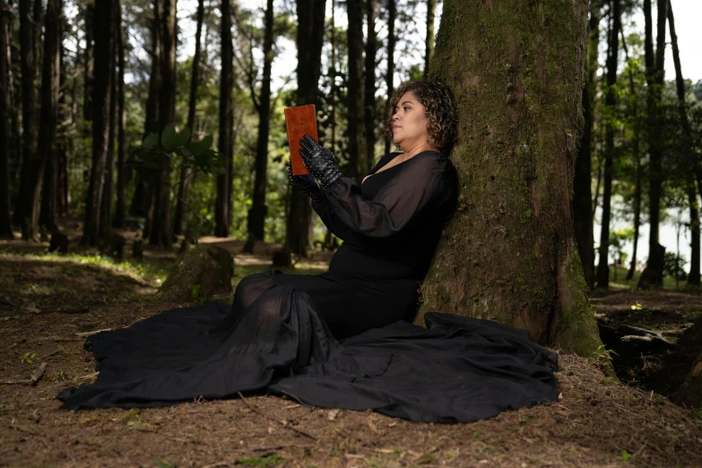 a woman is sitting under a tree holding an orange object