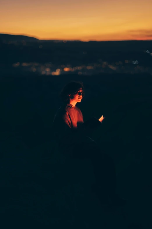 a man sitting on a hillside with the sun setting in the background