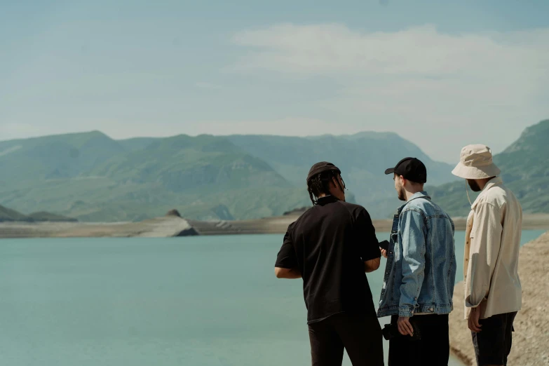 four men stand near the water in front of mountains