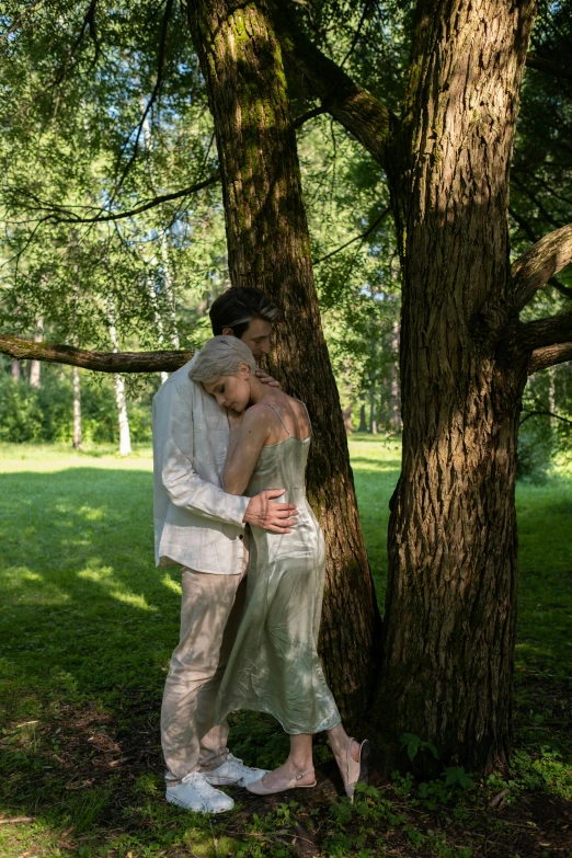 a bride and groom are hugging by a tree