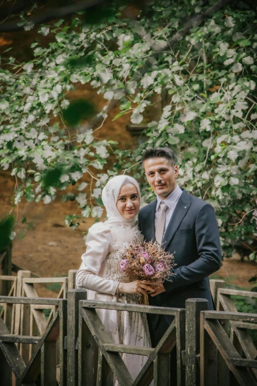 a couple standing together on a bridge next to some trees