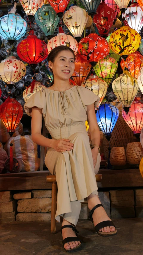 an asian lady sitting on a bench in front of a display of paper lanterns