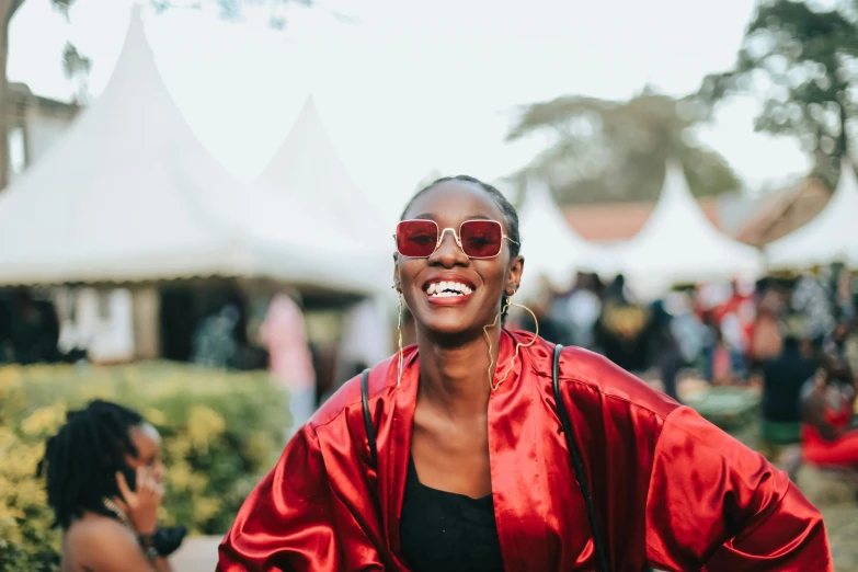 a woman in a red jacket smiling with other people and tents behind her