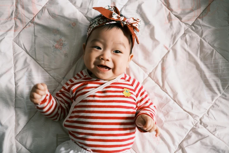 baby in striped shirt on white sheet with pink headband