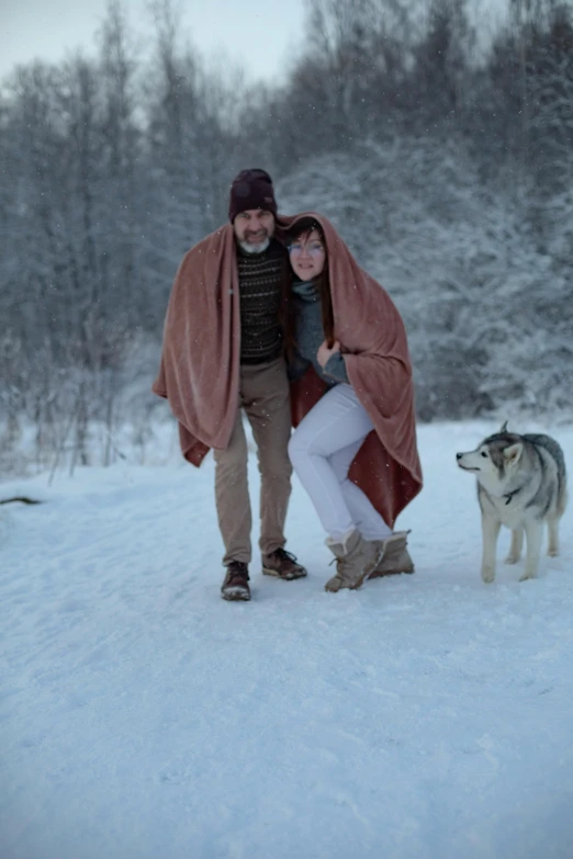 a man and a woman are standing in the snow with a wolf behind them